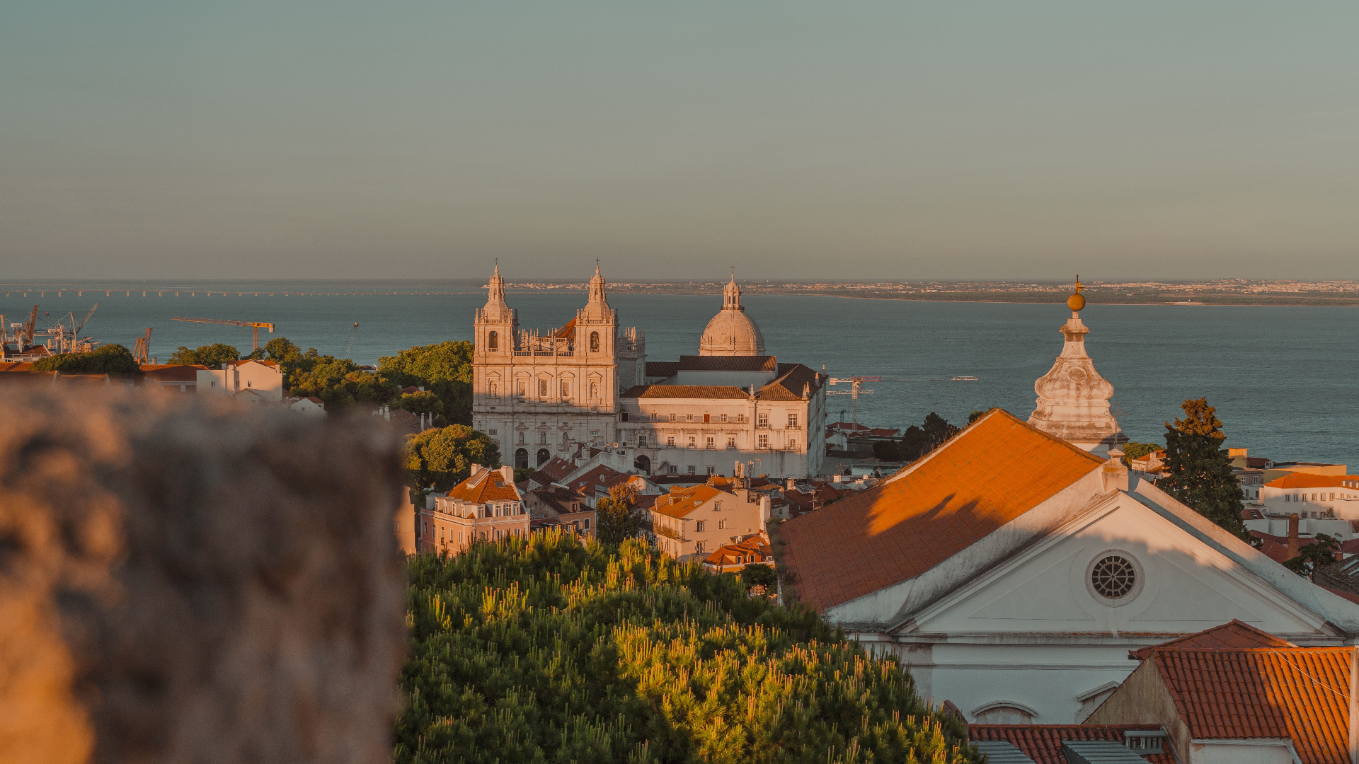 Sunset over Lisbon's terracotta rooftops, with São Vicente de Fora and the Tagus river in the distance
