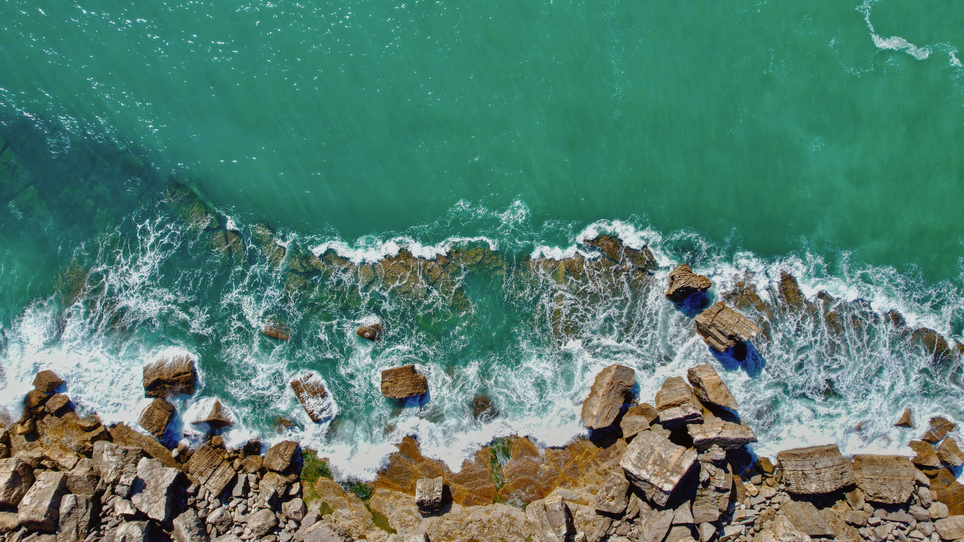 Aerial view of turquoise waves breaking over a rocky coastline
